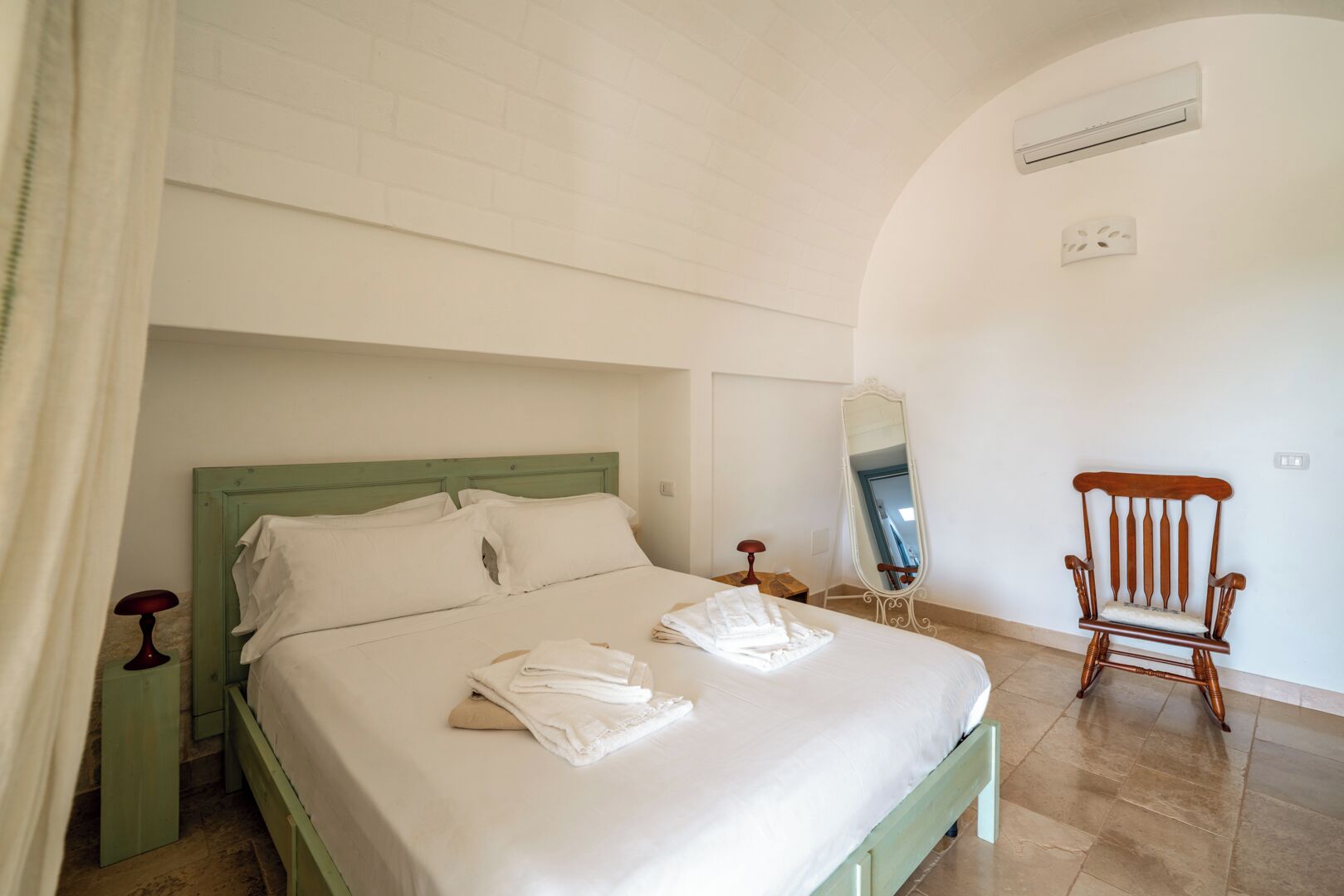 Quarto com cama, uma cadeira, espelho e aparelho de ar condicionado.