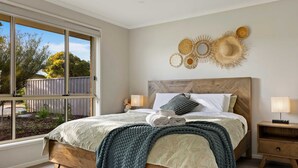Quarto com uma janela grande, cama de madeira, mesa de cabeceira e decoração na parede.