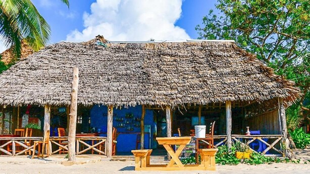 Eine rustikale Holzhütte mit einem Strohdach, Holzbanken und einem Tisch draußen.