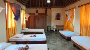Ein Zimmer mit drei Einzelbetten, Holzböden und orangefarbenen Vorhängen.