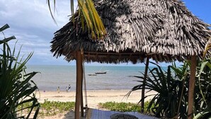 Eine Strandhütte mit einem Reetdach, einer Hängematte und Blick aufs Meer.