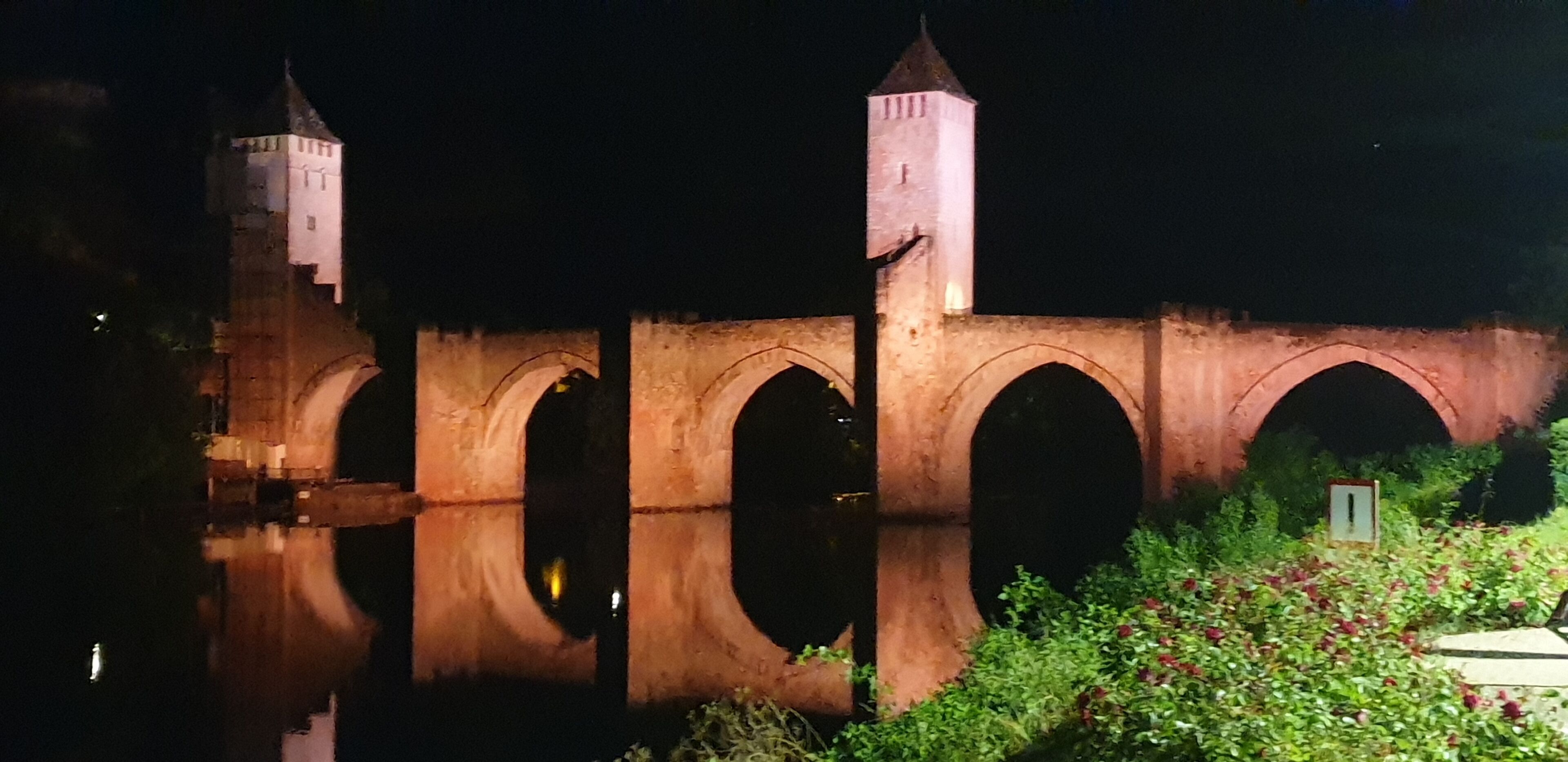 A historic stone bridge with arched passageways and two towers, illuminated at night.