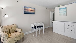 A compact room with a white desk, a chair, and a small table. There is a painting on the wall and a lamp on the left. - Harbour Beach Resort 219 (Daytona Beach)