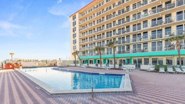 A hotel with a swimming pool, outdoor seating, and a multi-story building. - Harbour Beach Resort 219 (Daytona Beach)