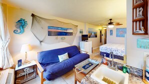 Una habitación con sofá azul, cama con vistas, televisión, lavabo y ventilador de techo.