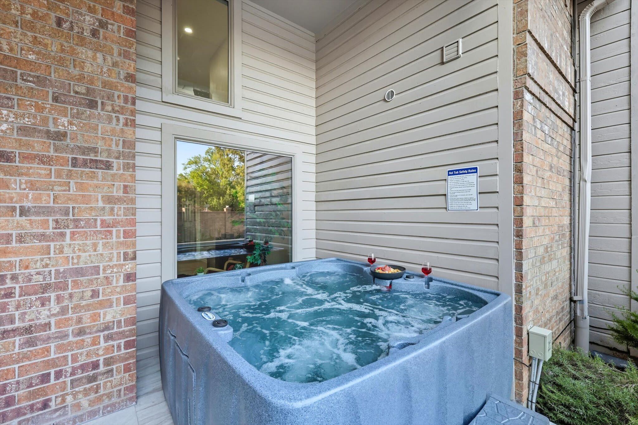 A hot tub outside a house with a brick wall and a window.