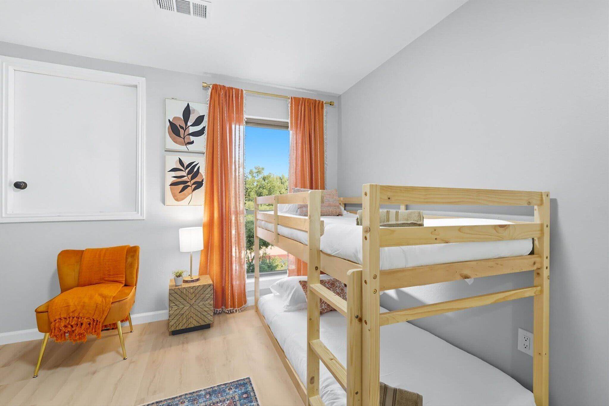 A room with a bunk bed, a chair, a side table, and artwork on the wall.