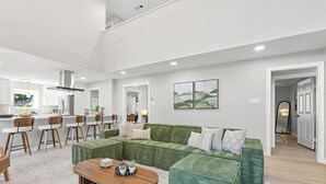 Un salón amplio con un sofá seccional verde, una mesa de centro de madera y una cocina al fondo.