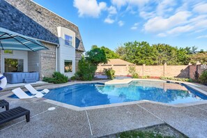 A backyard with a swimming pool, lounge chairs, and a patio area. - 7BR 5BA w Pool, Hot Tub, Sport Court & Game Room (DeSoto)
