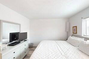 A bedroom with a bed, a TV on a dresser, a bedside table, and a window with blinds. - Atlantico 32 (Daytona Beach)