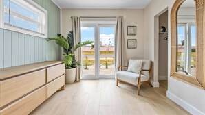 A room with a wooden bench, a potted plant, a sofa, a large mirror, and a sliding glass door leading to an outdoor area. - Welcome to The Drift Your Laid-back Beach Escape in Cocoa Beach! 2/2 (Cocoa Beach)