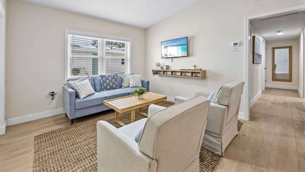 A living room with a blue sofa, beige armchairs, a wooden coffee table, and a TV mounted on the wall. - Welcome to The Drift Your Laid-back Beach Escape in Cocoa Beach! 2/2 (Cocoa Beach)