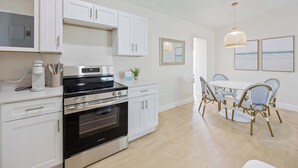 A modern kitchen with white cabinetry, a built-in oven, and a dining area with a white table and wicker chairs. - Welcome to The Drift Your Laid-back Beach Escape in Cocoa Beach! 2/2 (Cocoa Beach)