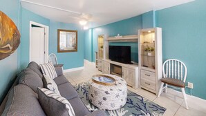 A living room with a sofa, a round coffee table, a television, and a white chair. - Ocean Jewels Club 104 - Beach Jewel (Daytona Beach)