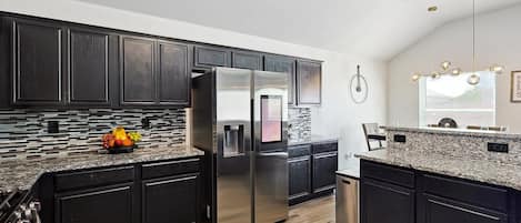 Una cocina moderna con armarios oscuros, un refrigerador de acero inoxidable, encimeras de granito y un frutero.