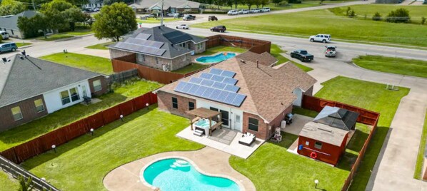 Un barrio residencial con una casa que tiene paneles solares, piscina y patio cercado.