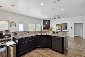 A modern kitchen with granite countertops, black cabinetry, and a built-in dishwasher. - 5BR Getaway in Desoto With Pool, Hot Tub & Cinema (DeSoto)