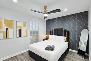 Un dormitorio moderno con cama, ventilador de techo, obras de arte en las paredes y un espejo grande.