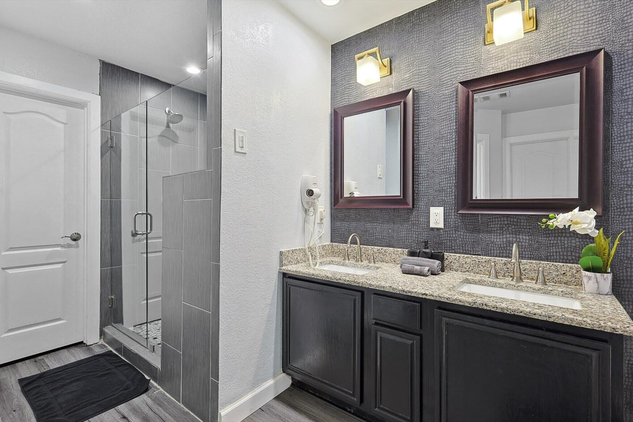 Une salle de bain moderne avec une douche à l’italienne, des meubles sombres et un comptoir en granit.