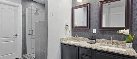 Une salle de bain moderne avec une douche à l’italienne, des meubles sombres et un comptoir en granit.