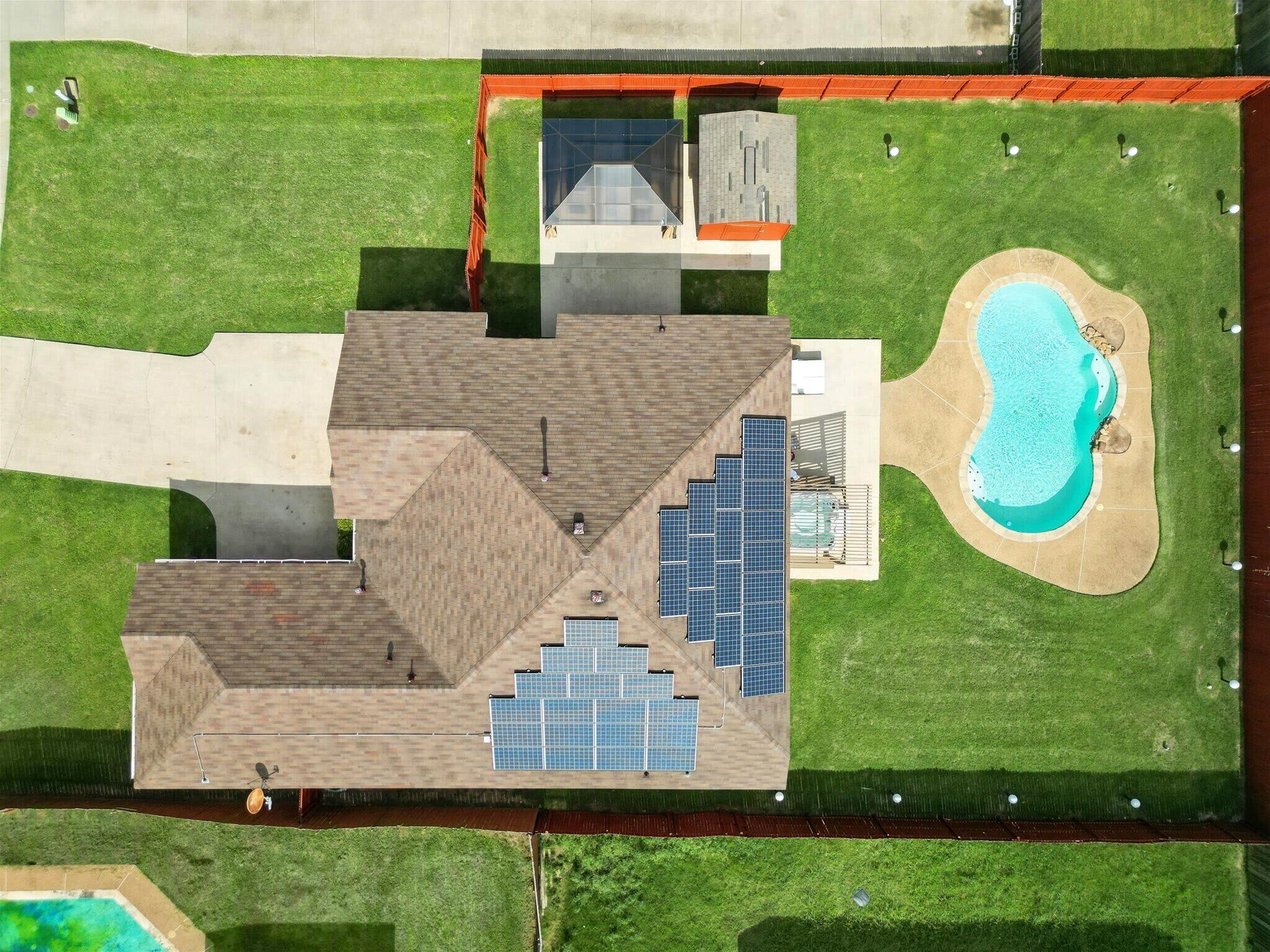 An aerial view of a modern building with a swimming pool, solar panels, and a well-maintained lawn.