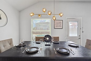 A dining room with a dark wooden table set for four, a chandelier, and a window with blinds. - 5BR Getaway in Desoto With Pool, Hot Tub & Cinema (DeSoto)