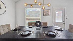 A dining room with a dark wooden table set for four, a chandelier, and a window with blinds. - 5BR Getaway in Desoto With Pool, Hot Tub & Cinema (DeSoto)