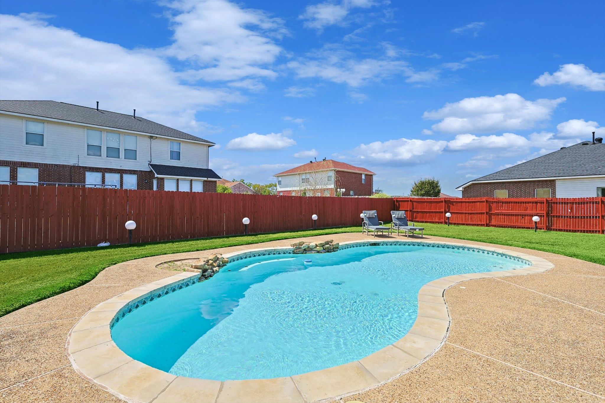 Patio con piscina, cerca de madera y casas al fondo.