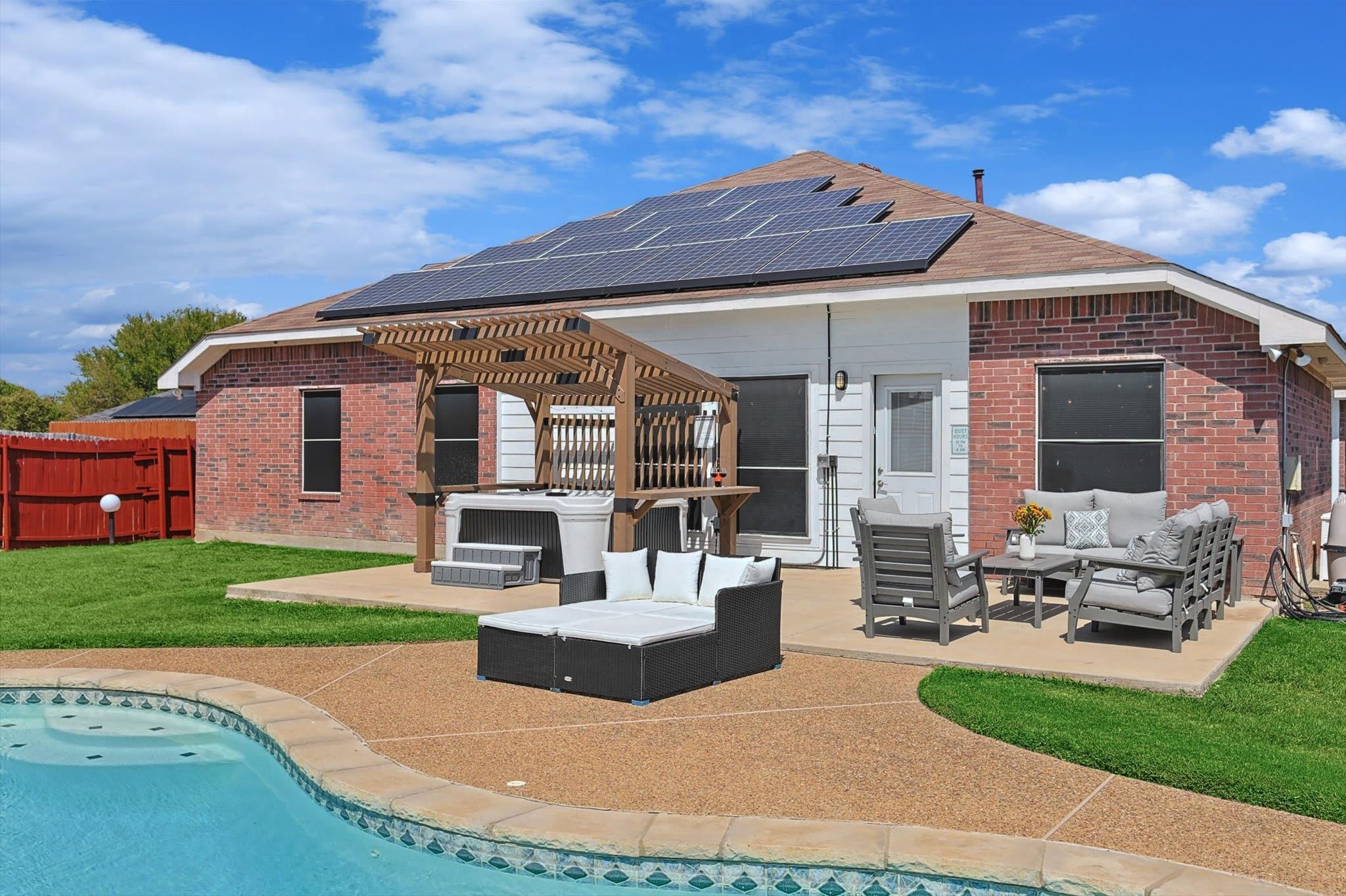 A house with a backyard patio, a swimming pool, and solar panels on the roof.