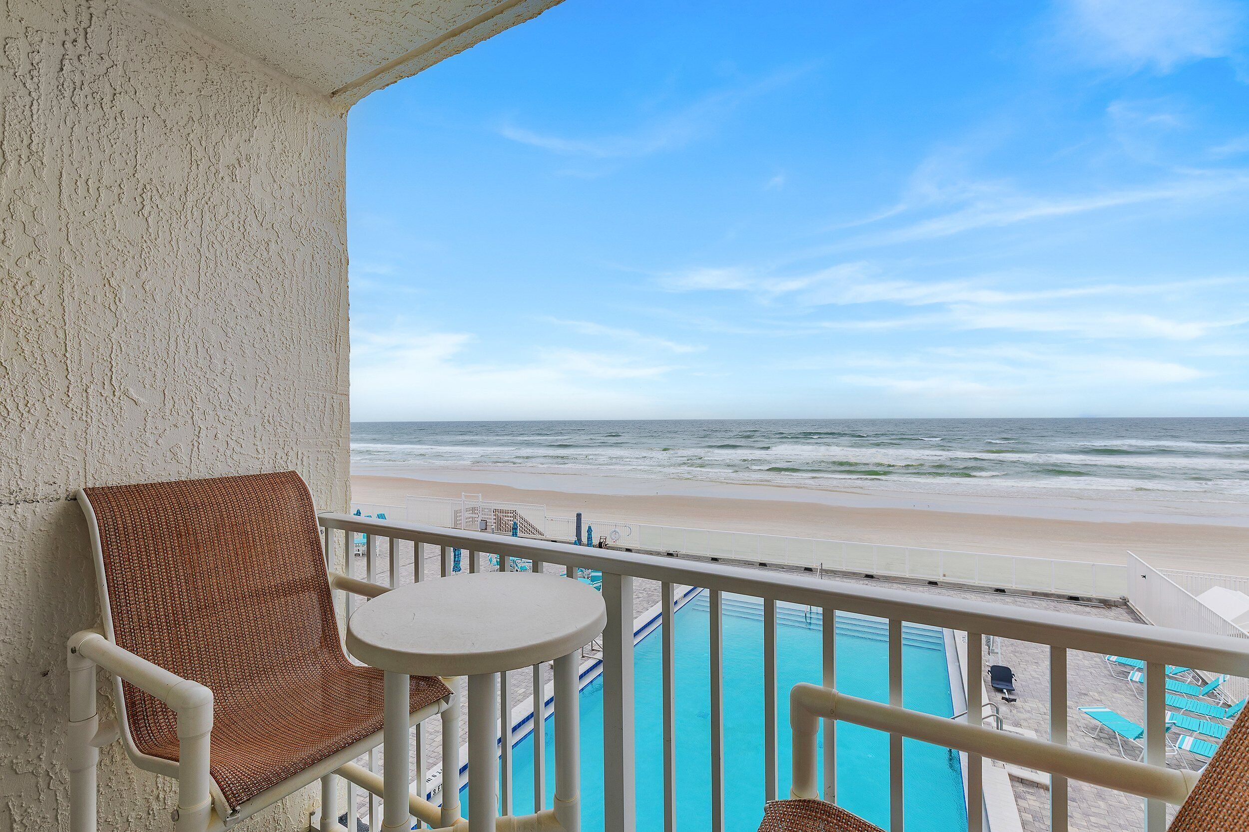 A balcony with a view of the beach and a pool.