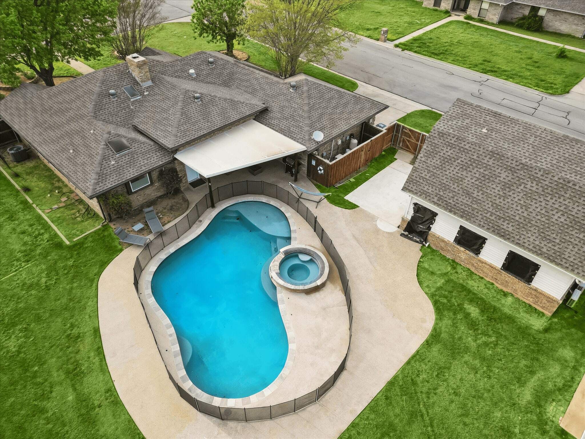 A residential property with a swimming pool, a covered patio, and a fenced backyard.