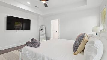A modern bedroom with a bed, a ceiling fan, a TV, a mirror, and a door.