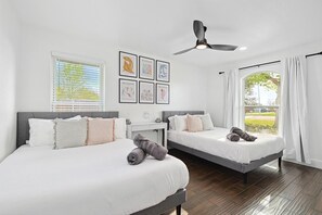 Ein Hotelzimmer mit zwei Betten, einem Deckenventilator, einem Fenster mit Jalousien und einem Bild an der Wand.