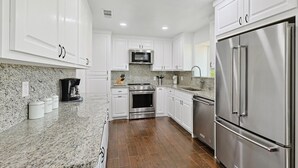 A kitchen with white cabinets, stainless steel appliances, granite countertops, and a wooden floor. - Gorgeous 4BR Home With Huge Yard, Pool (Denton)