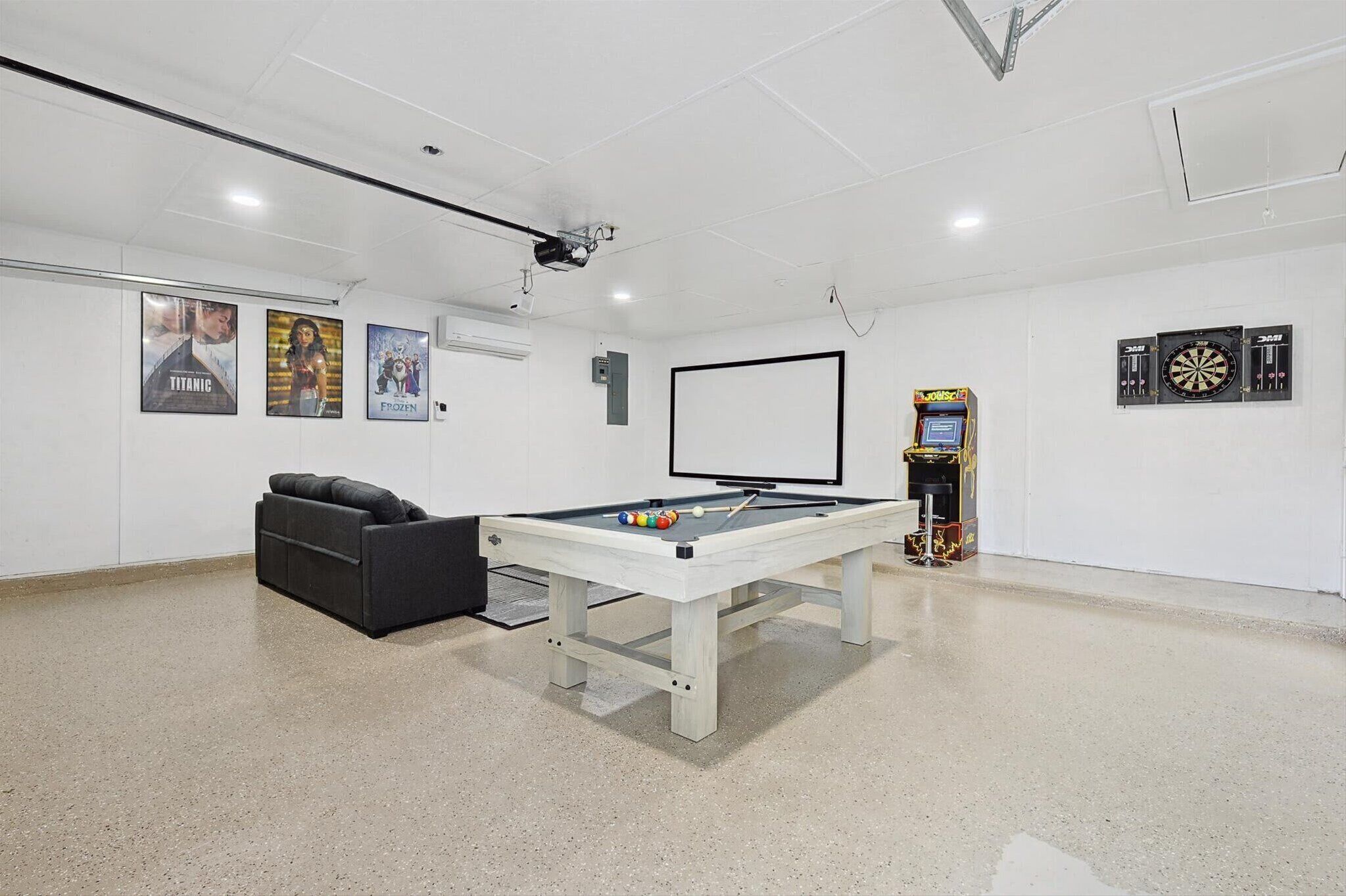 Een pooltafel met biljartballen, een bank, een dartbord en filmposters aan de muur.