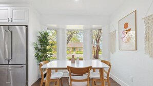 A kitchen with a stainless steel refrigerator, a dining table with four chairs, and a large window with a view of the outdoors. - Gorgeous 4BR Home With Huge Yard, Pool (Denton)