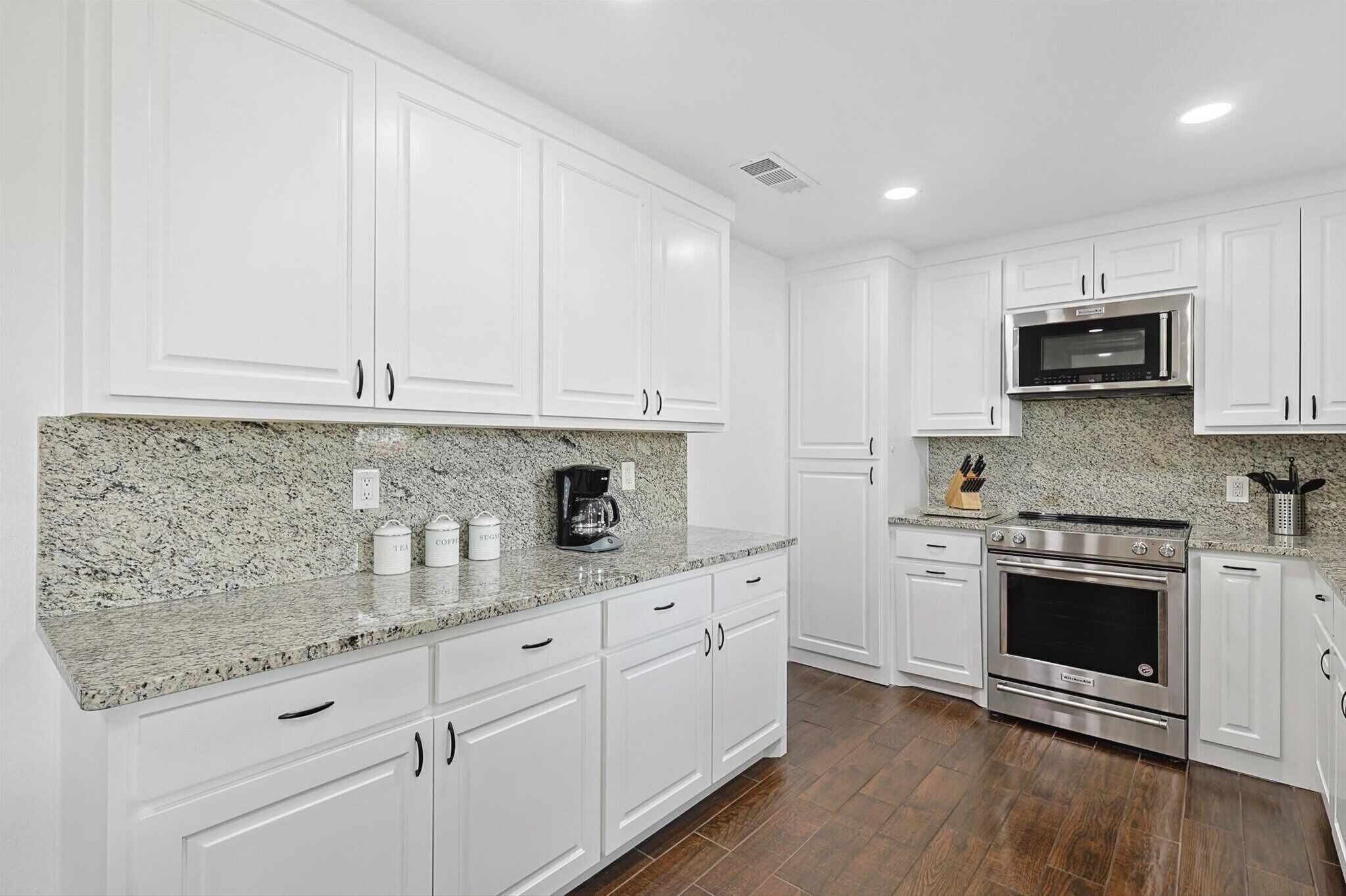 A kitchen with white cabinets, granite countertops, a stainless steel oven, and a microwave.