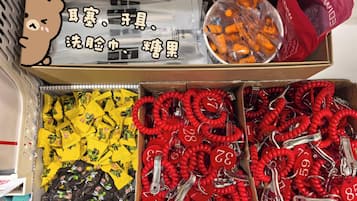 En kasse med forskellige ting, herunder snacks i gul og sort emballage, røde nøgleringe med tal, og orange genstande i plastic.