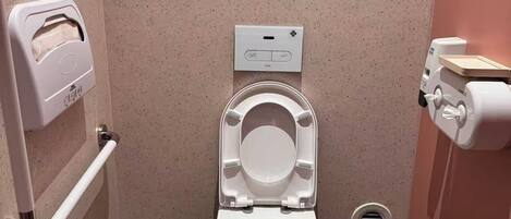 A modern bathroom with a white toilet, a hand dryer, a trash bin, and a soap dispenser.