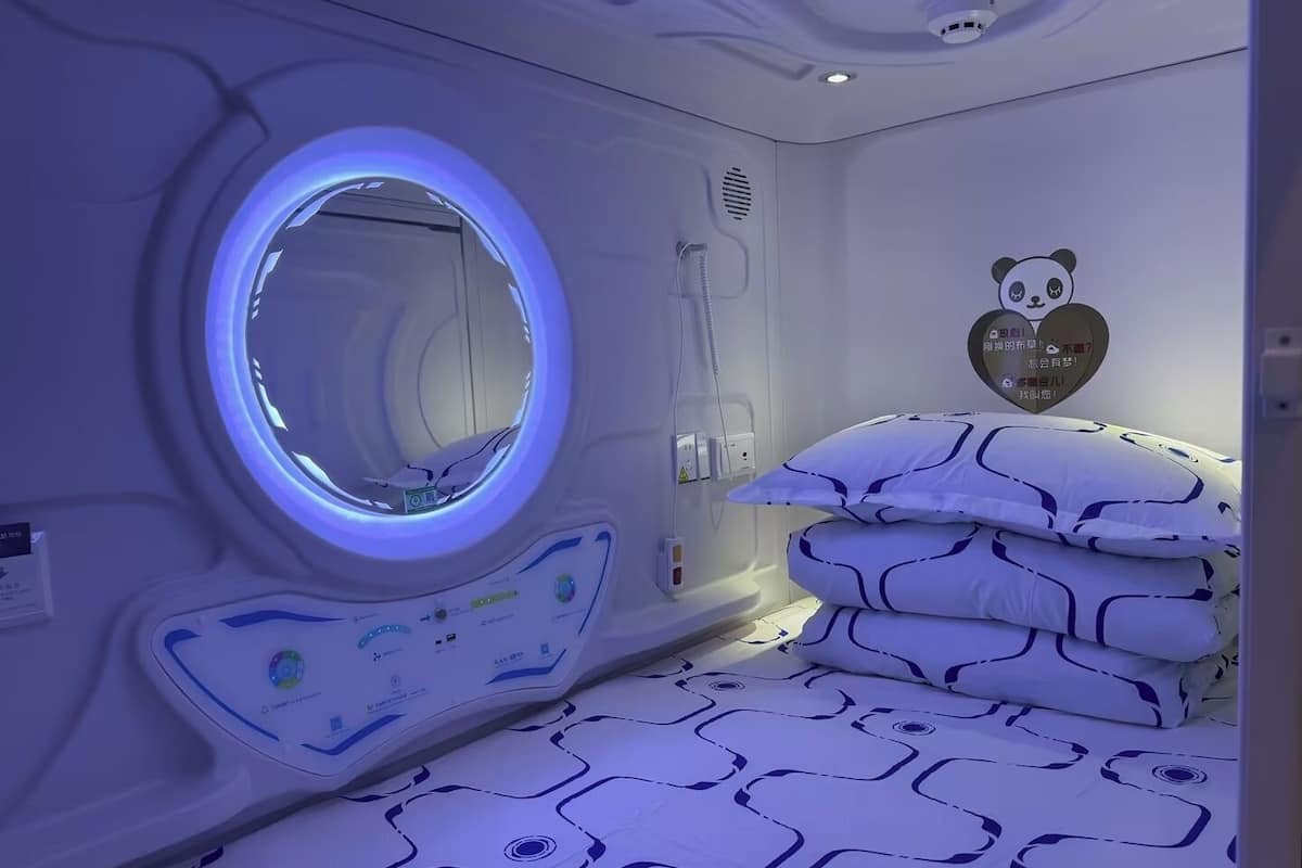 A room with a circular window, a bed with patterned bedding, and a wall-mounted panda decoration.