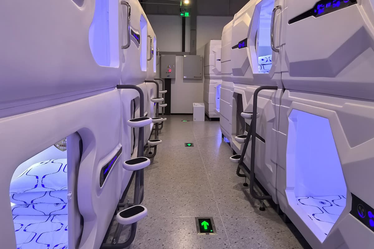 A row of futuristic, white restrooms with blue lighting accents and a tiled floor.