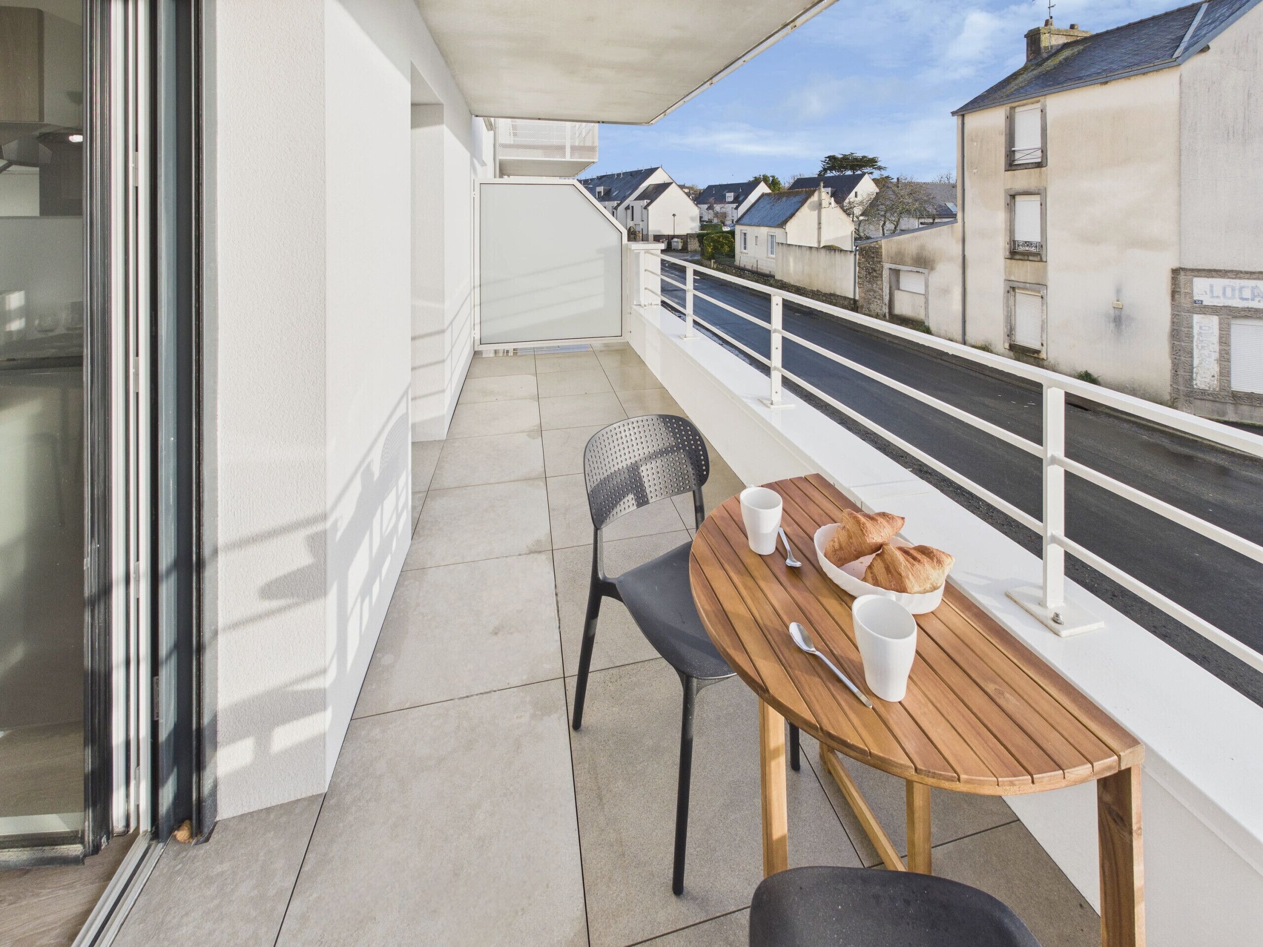 Ein Balkon mit Holztisch und -stühlen, einem weißen Geländer und Blick auf Wohnhäuser.