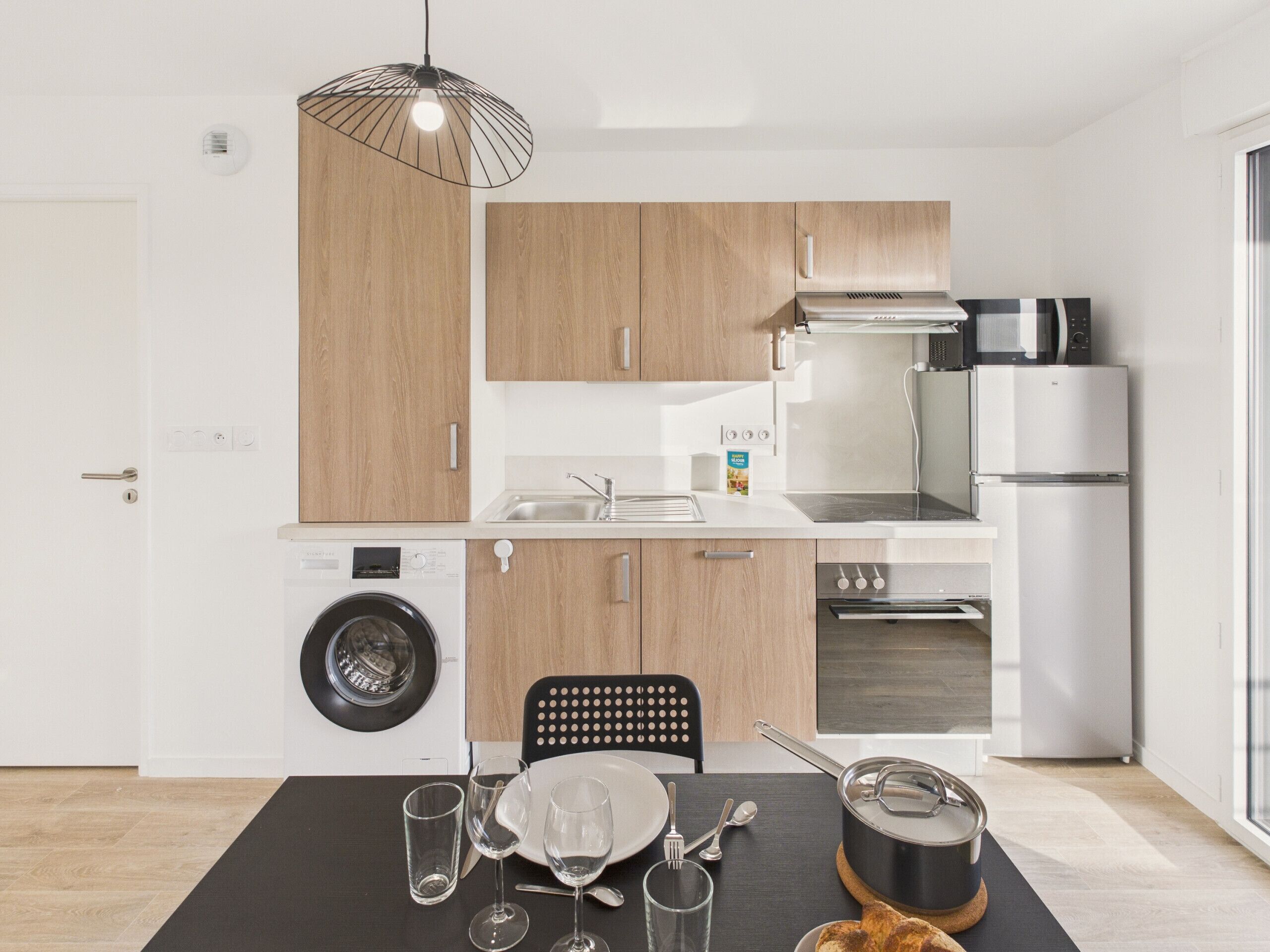 Une cuisine moderne avec des meubles en bois, un lave-linge, un four à micro-ondes et un réfrigérateur.