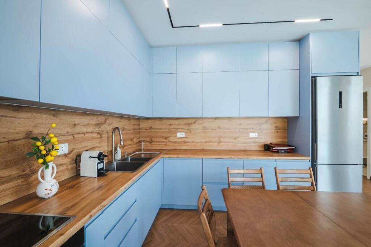 A modern kitchen with blue cabinets, a wooden countertop, a stainless steel refrigerator, and a dining table with chairs.