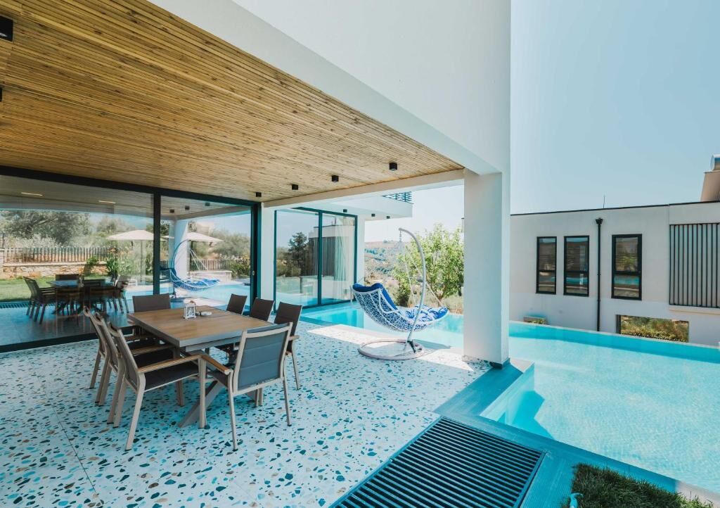 A modern outdoor patio with a pool, a dining area, and a swing chair.
