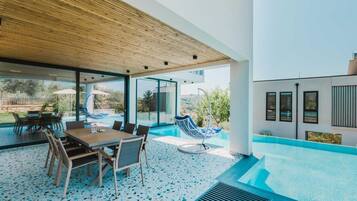A modern outdoor patio with a pool, a dining area, and a swing chair.