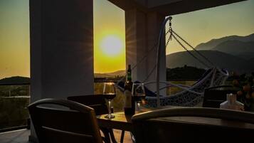 A terrace with a hammock, a table with wine glasses, and a view of the sunset over mountains.