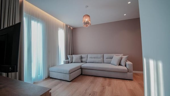 A modern living room with a sectional sofa, a flat-screen TV, and a wooden floor.