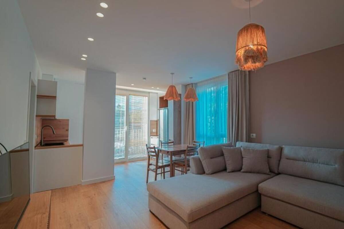 A modern living room with a sectional sofa, a dining table with chairs, and a large window with curtains.