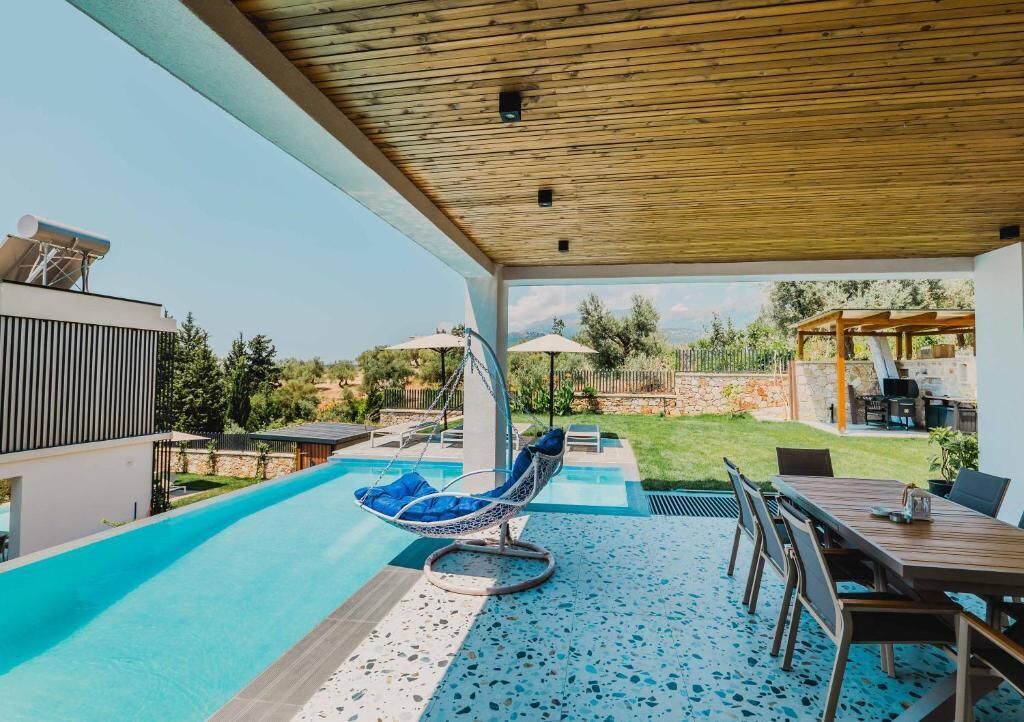 Un espacio exterior techado con piscina, una silla colgante y una mesa de comedor.